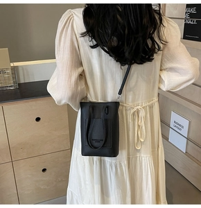 Vertical black litchi grain leather mini crossbody bag with embossed logo on model
