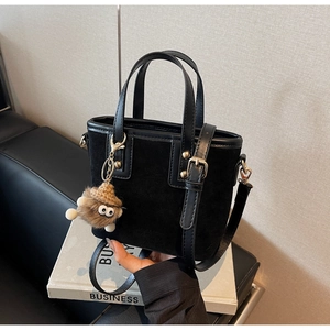 Détail du sac seau noir avec breloque monstre posé sur des livres de business