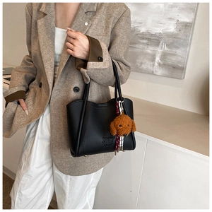Détail du sac seau noir en cuir grainé avec charme de chien en peluche et texte