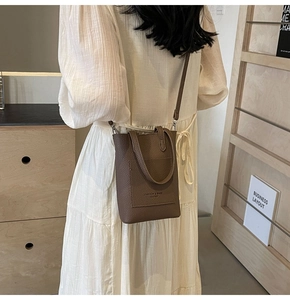 Close-up of brown litchi pattern leather mini bucket bag worn by model in casual setting