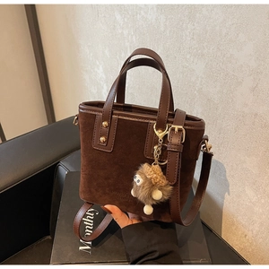 Détail du sac seau en daim marron foncé avec poignées en cuir et breloque peluche