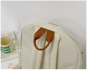 Close-up of cream canvas backpack featuring brown PU handle and sturdy back straps
