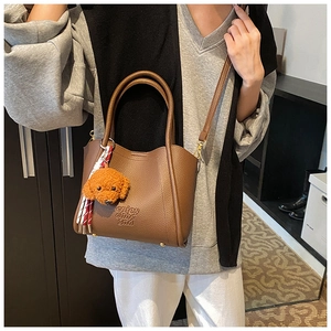 Détail d'un sac seau en cuir litchi marron avec pendentif chien et ruban élégant