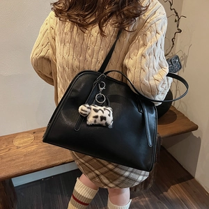 Détail d'un sac cabas en similicuir noir avec un charme décoratif en peluche vache