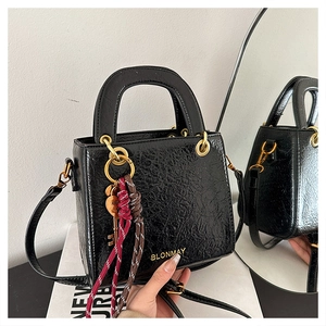 Close-up of black glossy leather handbag with gold logo and woven keychain detail