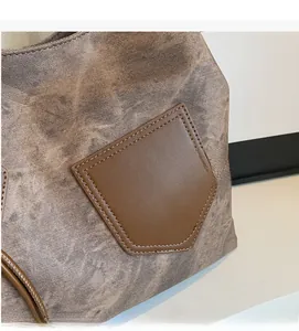 Detail of gray canvas tote bag with brown faux leather pentagon pocket and neat stitching