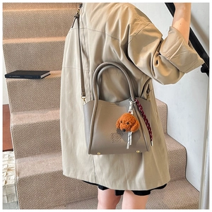 Detail of grey bucket bag with textured leather, brown strap and a cute puppy plush charm