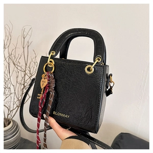 Detail of black glossy wrinkled leather bag with gold hardware and woven heart charm