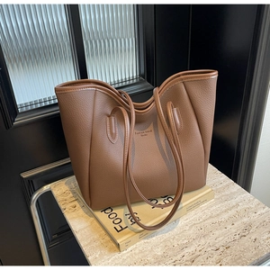 Close-up of brown pebbled leather tote bag featuring elegant brand text on marble surface