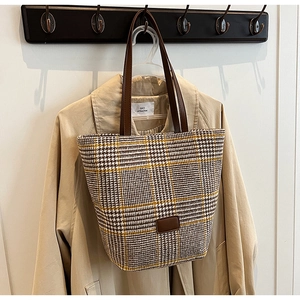 Dettaglio borsa tote in tweed pied de poule giallo e marrone con manici in pelle su un trench