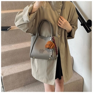Détail d'un sac en cuir gris avec pendentif chien en peluche et glands décoratifs