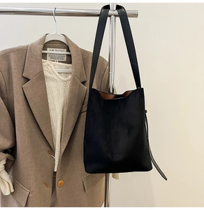 Detail of a black suede tote bag with brown lining hanging against an elegant outfit