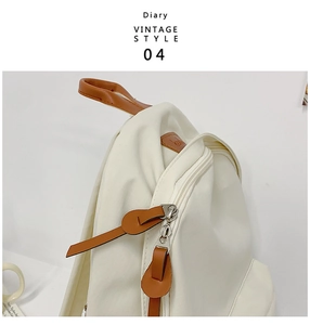 Detail of white canvas backpack featuring brown leather zipper pulls and vintage style logo