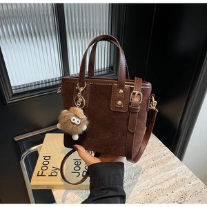 Détail du sac seau en daim marron café avec ferrures dorées et breloque pelucheuse douce