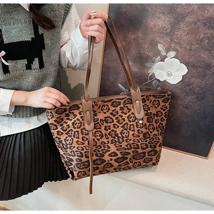 Detail of leopard print tote bag with brown handles held by a model in warm light