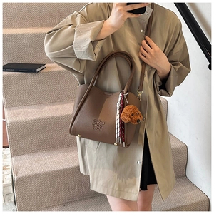 Détail du sac seau en cuir marron avec peluche de chien et foulard sur l'escalier