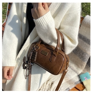Borsa Boston vintage marrone con targa dorata e ciondoli su una panchina