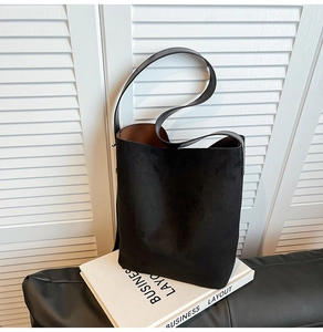 Detail of minimalist black suede bucket bag with wide shoulder strap and tan inner lining