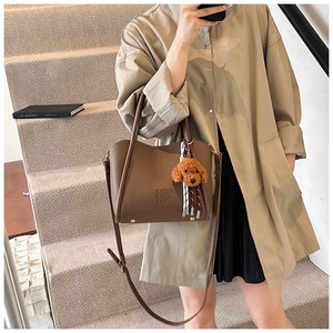 Détail du sac seau en cuir marron avec charm peluche sur des escaliers