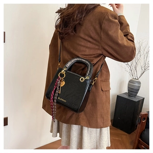 Detail of black glossy embossed leather handbag with silk scarf on a model