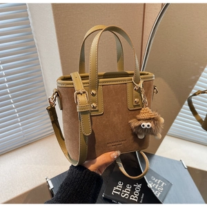 Détail d'un sac cabas en daim marron et cuir vert olive avec charm monstre en peluche