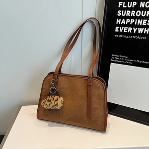 Détail d'un sac cabas en daim marron avec pompon léopard et anses en cuir