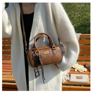 Dettaglio borsa Boston in pelle marrone con finiture dorate e ciondolo a gatto su una panchina