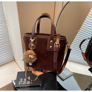 Détail du sac seau en daim marron foncé avec poignées en cuir et charm en peluche