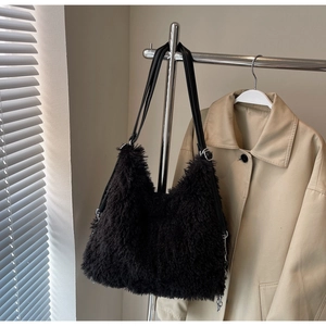 Close-up of black fuzzy plush shoulder bag with long straps hanging in a minimalist room