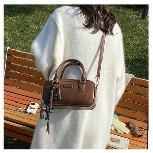 Dettaglio borsa Boston in pelle marrone con logo dorato e ciondolo a forma di cioccolato