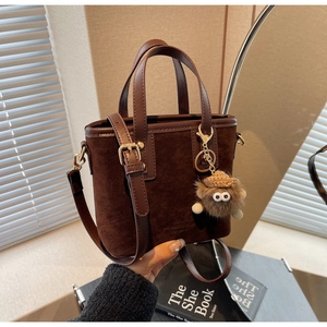 Vue détaillée du sac seau en daim marron café avec charme en peluche et bandoulière cuir