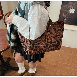 Detail of leopard print tote bag with brown leather handles on shoulder of a model