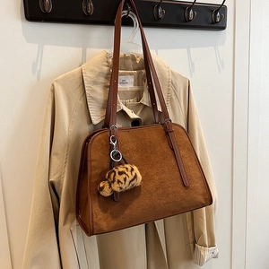 Détail du sac cabas en daim marron avec pendentif léopard sur un trench-coat beige clair