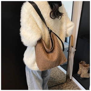 Detailed view of a brown plush hobo bag with black leather shoulder strap on a model