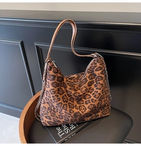 Close-up of leopard print hobo bag with leather strap and chain detail on wooden chair