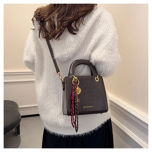 Detail of dark brown leather handbag with gold logo, heart charm and plaid scarf accent