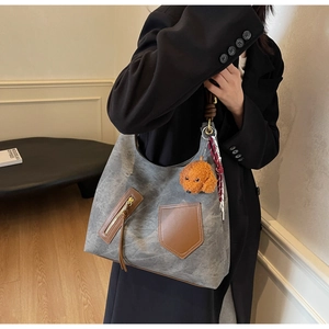 Detailed view of grey canvas tote with leather accents, plush charm and striped scarf