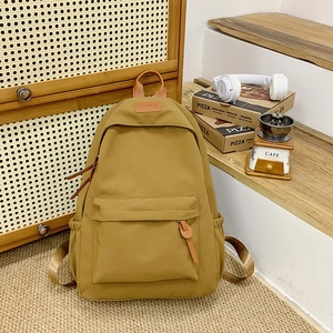 Detail view of khaki school backpack with leather handle and side pockets on a rug