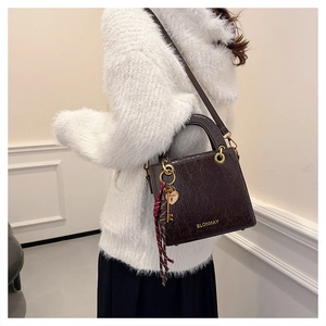 Detail of dark brown square handbag with pleated leather texture and heart charm