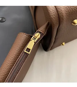 Detail of brown lychee leather handbag showing smooth side zipper and metal bottom studs