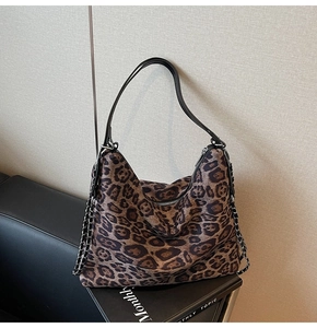 Detail of leopard print tote bag featuring black leather strap and metal chain trim