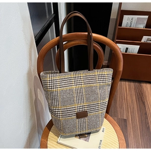 Détail d'un sac cabas à carreaux avec anses en cuir marron posé sur une chaise en bois