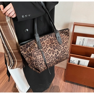 Detail of leopard print tote bag with black leather handles in a cozy indoor setting