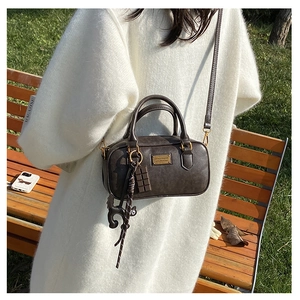 Borsa Boston vintage marrone con placca oro e ciondolo gatto su maglione bianco