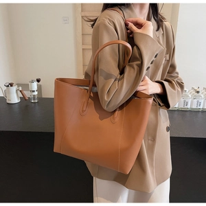 Detail of a large brown faux leather tote bag featuring visible stitching and dual handles