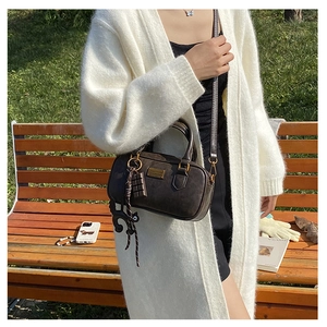 Dark brown retro pillow bag with cat charm on a park bench in soft sunlight