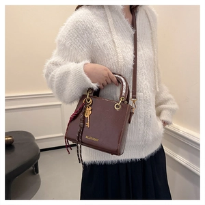 Close-up of brown glossy handbag with woven tassel and metallic key charm details