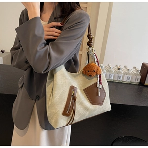 Detail of canvas tote bag featuring brown leather pockets and a cute teddy bear charm