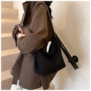 Detail of black fuzzy hobo bucket bag on model with brown trench coat in indoor setting