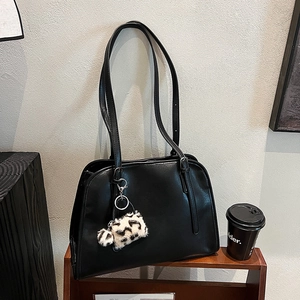 Détail d'un sac cabas en cuir noir avec breloque léopard sur une étagère en bois